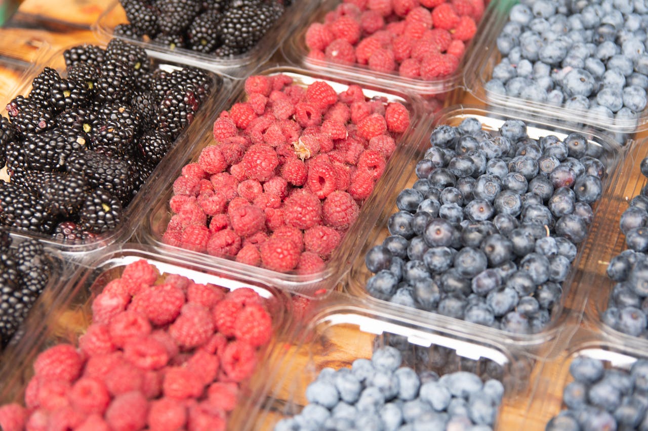 Close-up of assorted fresh blackberries, raspberries, and blueberries in clear containers.